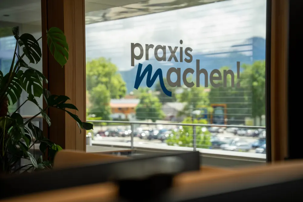 praxismachen! Logo am Fenster mit Blick über Murnau